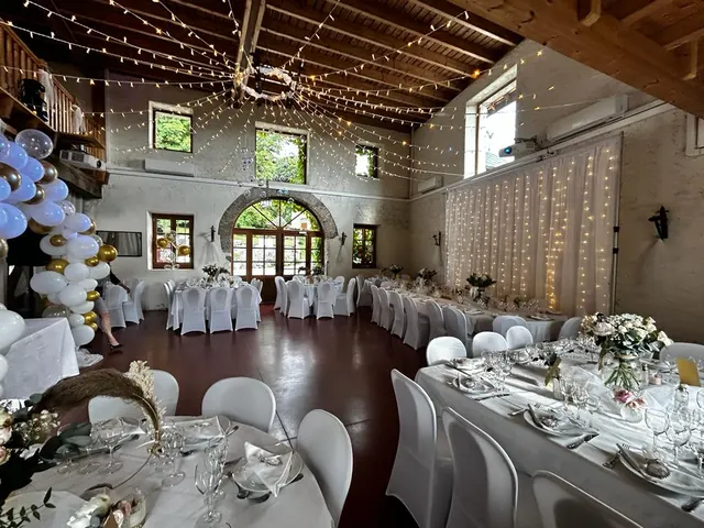 Salle de la dépendance dressée pour un dîner, guirlandes lumineuses au plafond et mezzanine en bois