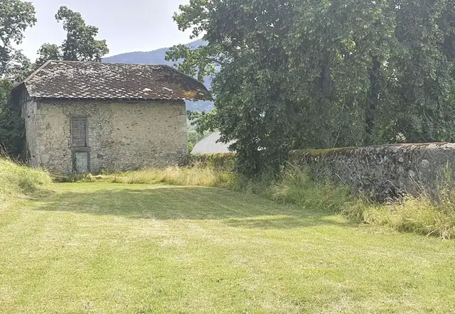 Grande pelouse plate au pied d’une grange en pierre, réservée aux tentes des invités