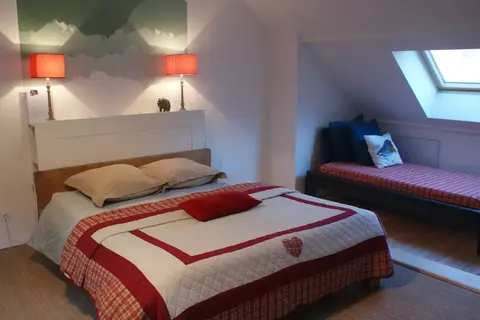 Chambre mansardée avec lit double et lit simple sous un velux