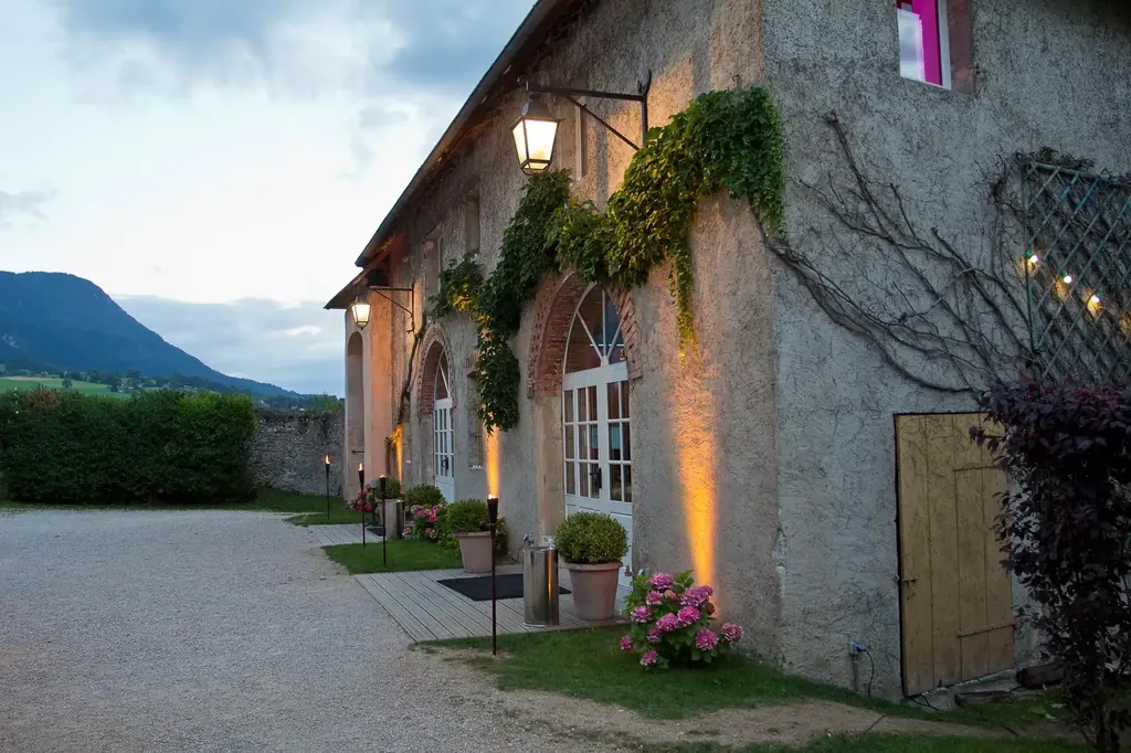 Façade en pierre du Château de Saint-Offenge illuminée au crépuscule, lanternes et hortensias roses